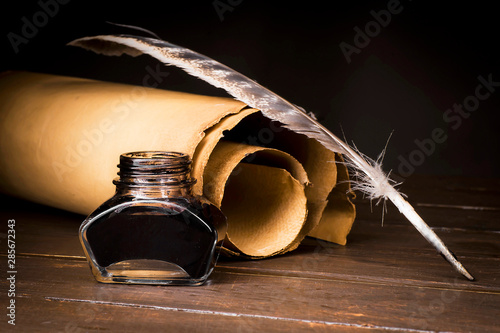 Parchment scrolls and inkwell with a pen on the background of boards photo