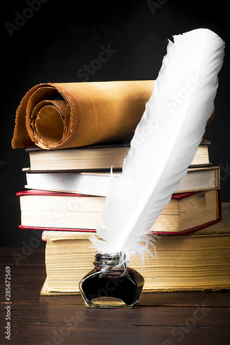 Scrolls of parchment with a pen and inkwell against the background of a pile of books