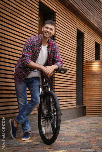 Fototapeta Naklejka Na Ścianę i Meble -  Handsome man with modern bicycle near building outdoors