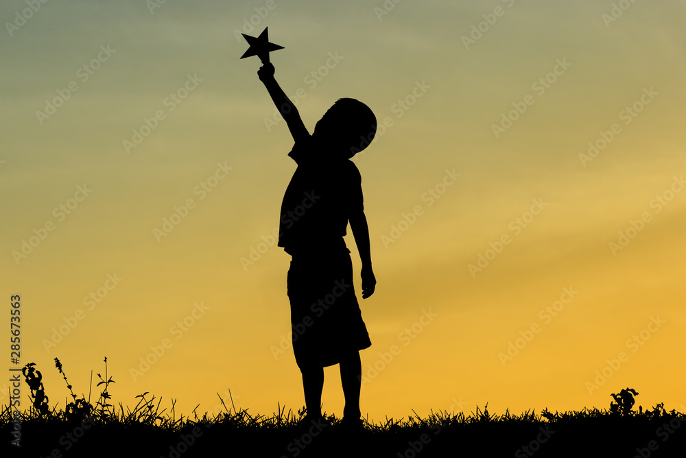 A silhouette of a little child reaching out to grab stars, Expresses the ambition, The joy of a small child with dreams. Kid having fun at sunset. Summer vacation and travel concept.