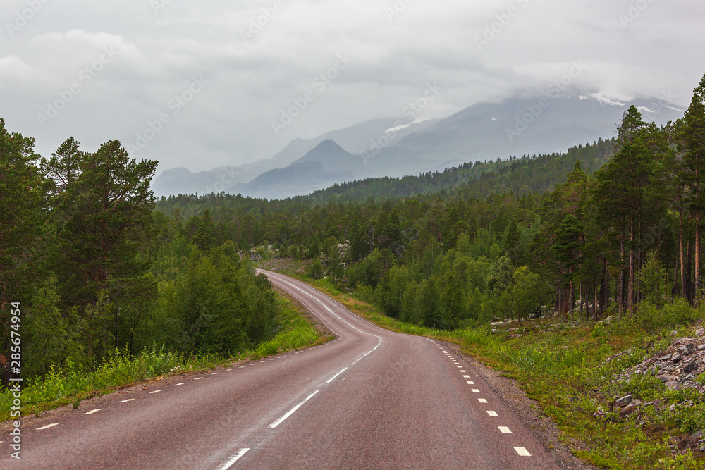 Road across Arctic Sweden with picturesque view of snow-covered tops of the mountains of Sarek national park
