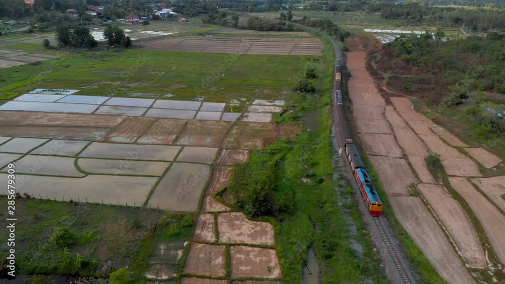 Aerial view, Locomotive Express Train traveling on a railway pass through green paddy fields of newly transplanted rice seedlings in green season at Chiang Mai, Thailand. Aerial view, Locomotive Express Train traveling on a railway pass through green paddy fields of newly transplanted rice seedlings in green season at Chiang Mai, Thailand.