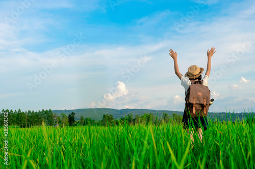 A happy girl enjoying nature in meadow. Outstretched arms, breathing fresh air with a cloudy blue sky in the background - concept of clean atmosphere.