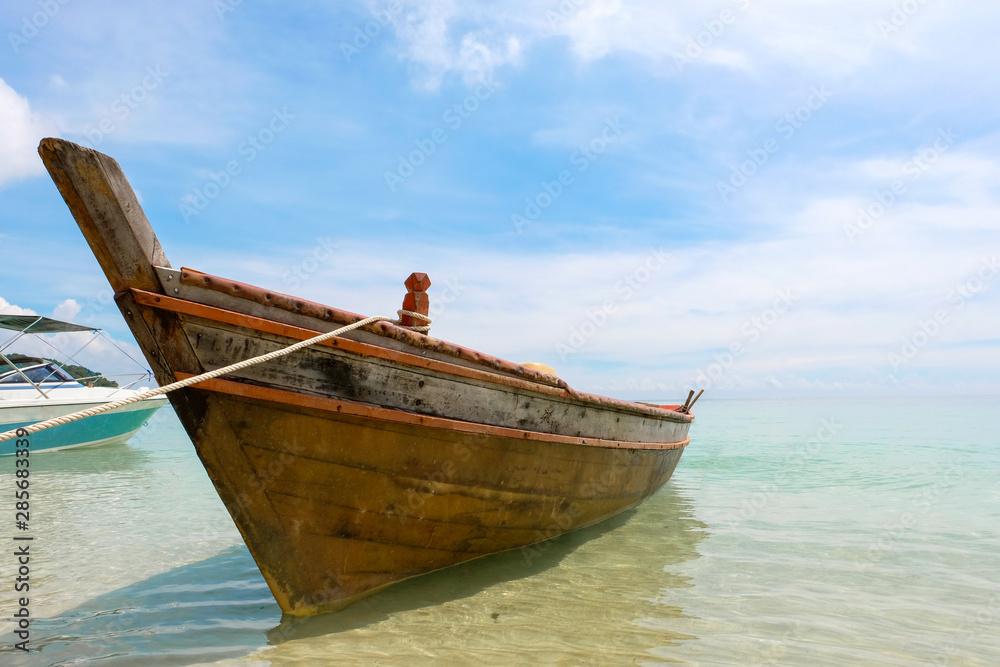Old wooden boat and blue sea under cloudy sky on white beach in sunny day.