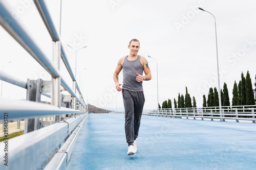 Portrait of a charming young slim male running around on a morning jog on a cloudy summer morning. Energy charge concept and burning calories. Copyspace © Rithor