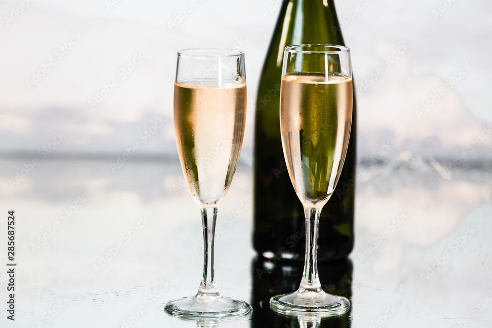 Party concept. Photo detail of two luxurious glass cups with yellow cava and a green bottle behind with the background illuminated by many small lights. Concept of celebration.