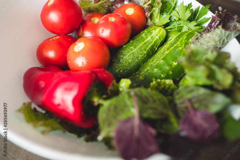 Fresh vegetables, tomatoes, cucumbers, lettuce, red peppers, and herbs in a plate on a rustic wooden table - rural style, healthy, organic food concept Fresh vegetables, tomatoes, cucumbers, lettuce, red peppers, and herbs in a plate on a rustic wooden table - rural style, healthy, organic food concept