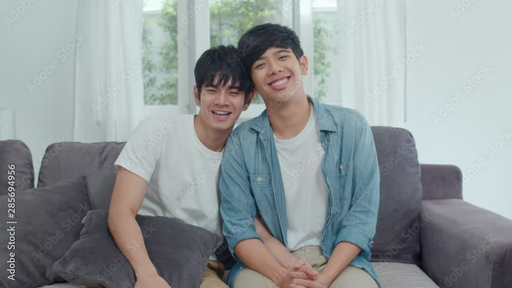 Portrait Young Asian Gay couple feeling happy smiling at home. Asian LGBTQ men relax toothy smile looking to camera while lying on sofa in living room at home in the morning concept. Portrait Young Asian Gay couple feeling happy smiling at home. Asian LGBTQ men relax toothy smile looking to camera while lying on sofa in living room at home in the morning concept.