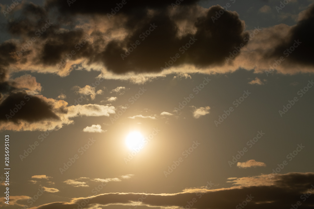 bright sun in an orange sky with dark clouds at sunset