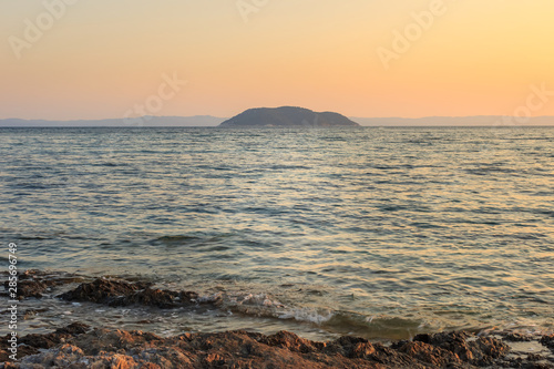 Foreground rocks and wavy sea in front of the Turtle island in Greece during sunset, viewed from the reef on Paradaisos beach in Neos Marmaras photo