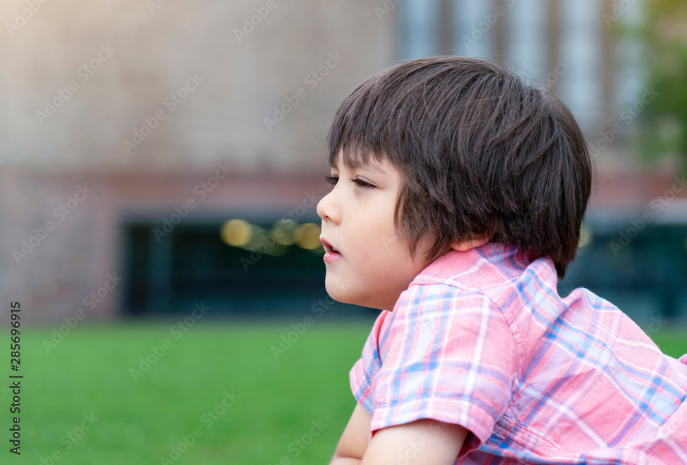 Side view portrait of little boy looking out with thinking face, Head shot Kid lying down on grass in the park, Child relaxing outside in weekend. Side view portrait of little boy looking out with thinking face, Head shot Kid lying down on grass in the park, Child relaxing outside in weekend.