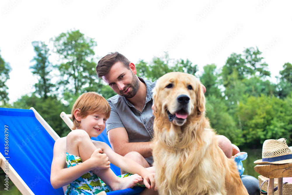 Man and young boy stroking Golden retriever on pier during summer weekend