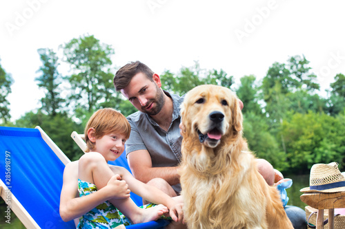 Man and young boy stroking Golden retriever on pier during summer weekend © moodboard