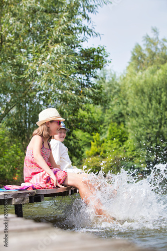 Fototapeta Naklejka Na Ścianę i Meble -  Kids playing water in lake while sitting on pier