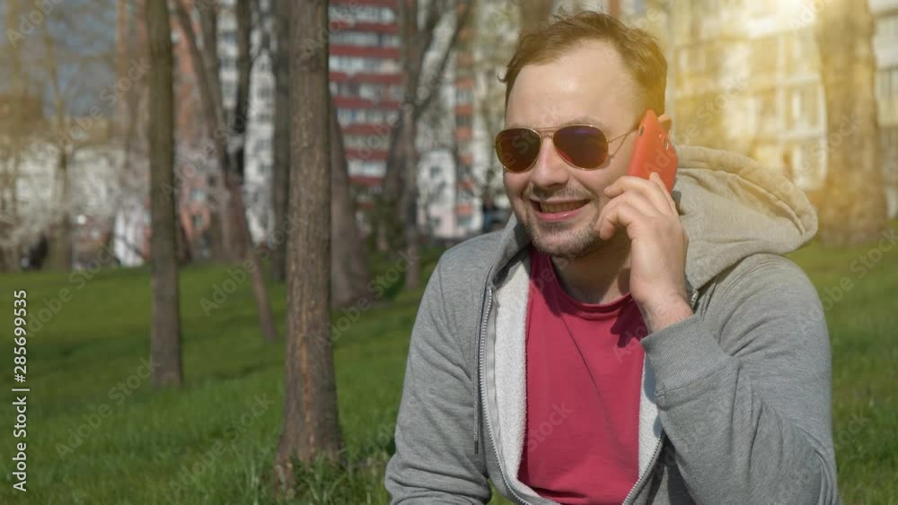 Guy talks on smartphone. Man with red smartphone in public garden, speaks and gesticulates Guy talks on smartphone. Man with red smartphone in public garden, speaks and gesticulates
