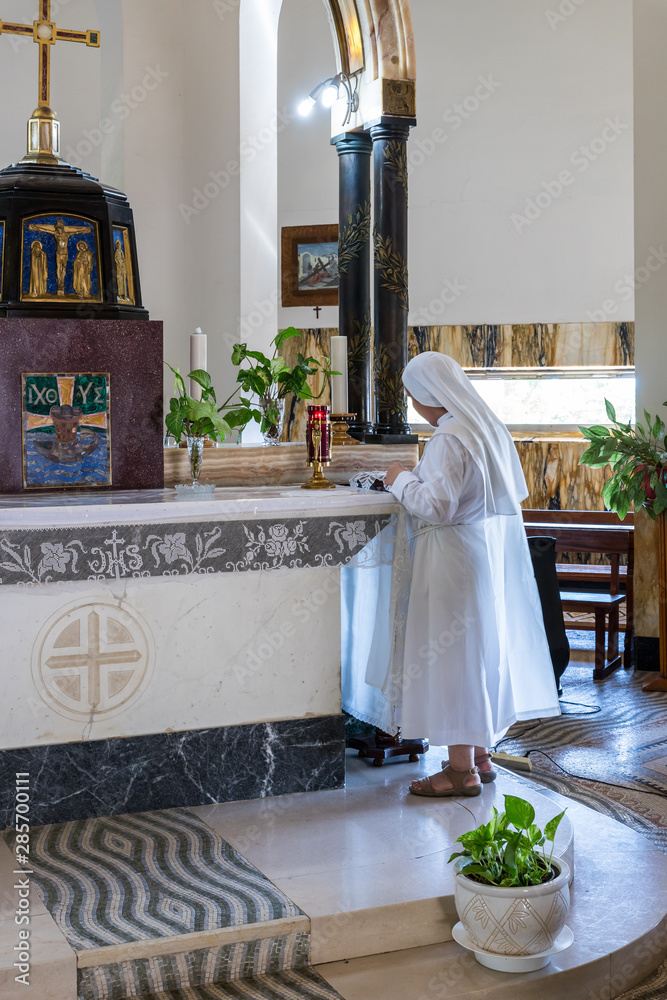 A monk nun in white robes prays in the central hall of the Beatitude ...