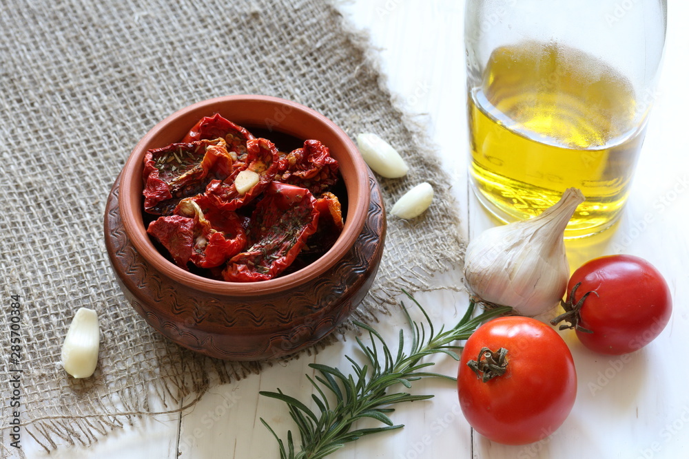 Sun-dried tomatoes with spices and garlic in a clay pot. Nearby is a bottle with olive oil, tomatoes, rosemary and garlic. Sun-dried tomatoes with spices and garlic in a clay pot. Nearby is a bottle with olive oil, tomatoes, rosemary and garlic.