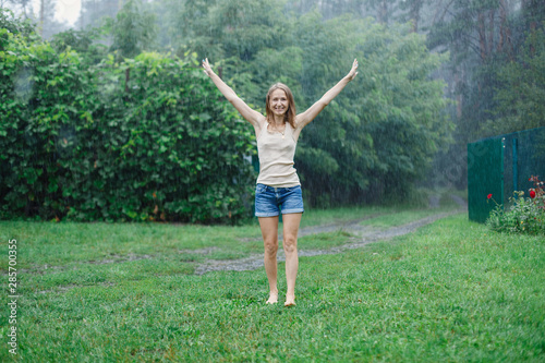 Happy smiling woman walking under summer rain. emotional girl wet in rain without umbrella on green nature background. young attractive woman damp in rain