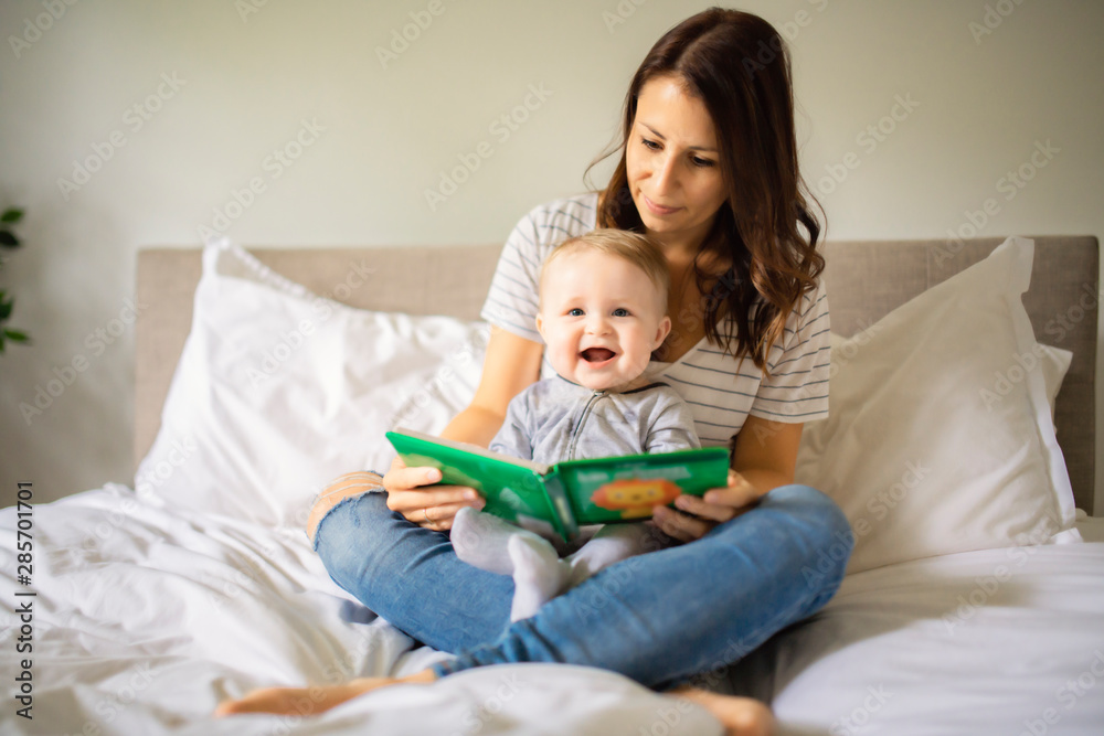 Mother and child on a white bed playing in sunny bedroom Mother and child on a white bed playing in sunny bedroom