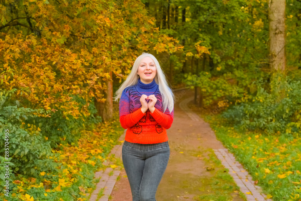 young pretty plus size caucasian woman in orange fashion sweater walks in autumn park