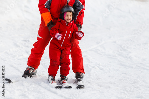 Professional ski instructor is teaching a child to ski on a sunny day on a mountain slope resort with sun and snow. Family and children active vacation.