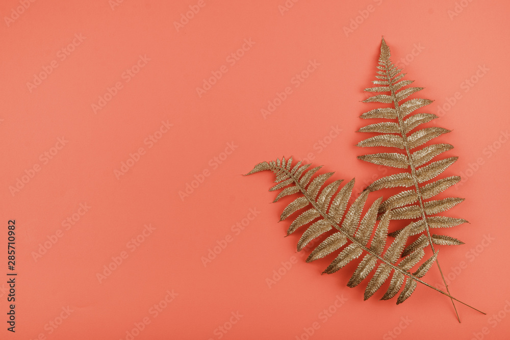 Golden palm leaves on coral background. Summer background with golden tropical leaves, copy space