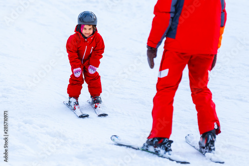 Professional ski instructor is teaching a child to ski on a sunny day on a mountain slope resort with sun and snow. Family and children active vacation.