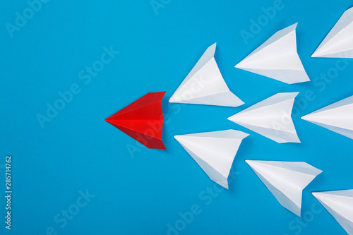 Group of white paper plane in one direction and one red paper plane pointing in different way on blue background. Business for innovative
