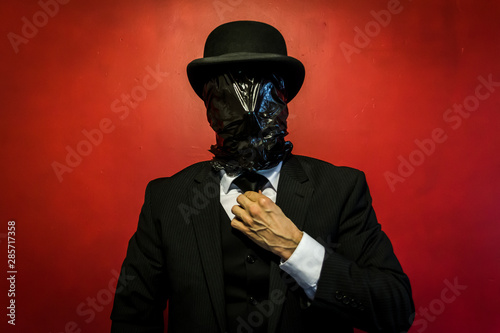 Fototapeta Portrait of Man in Dark Suit and Bowler Had With Black Plastic Bag Over His Face Straightening His Tie