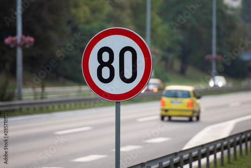 80km/h Speed limit sign a highway with small yellow car in the background