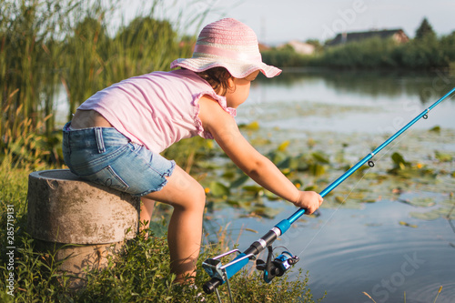 Sweet little girl on fishing near the river. Little girl, 4-5 years, spending fishing time alone on the river coast. Kids and fishing concept.