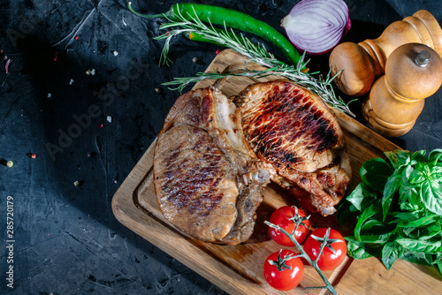 Grilled steak with herbs, spices and cherry tomatoes on dark background