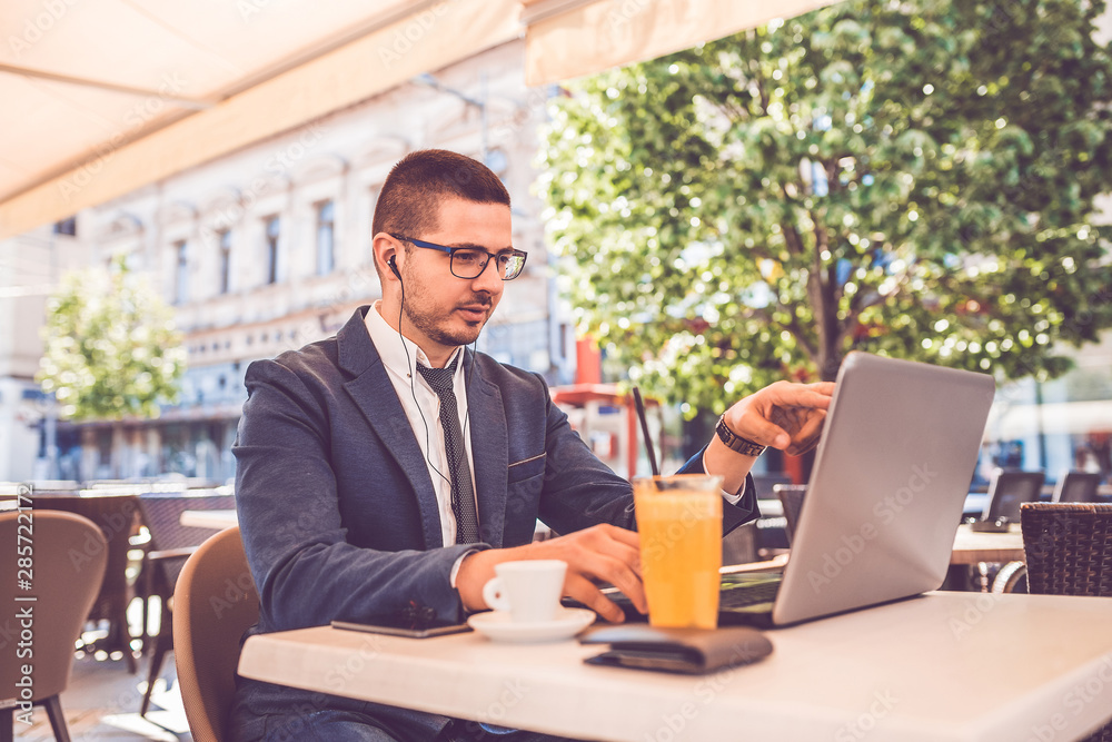 Young man sitting at street cafe having a conversation on a laptop wearing a headphones Young man sitting at street cafe having a conversation on a laptop wearing a headphones