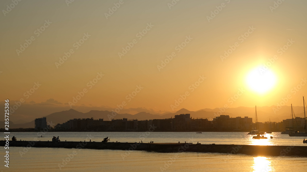 Colorful, golden sunset over the coastal city in the summer time. Nature beautiful background for tranquil and peaceful concept. Silhouettes of people on the pier.