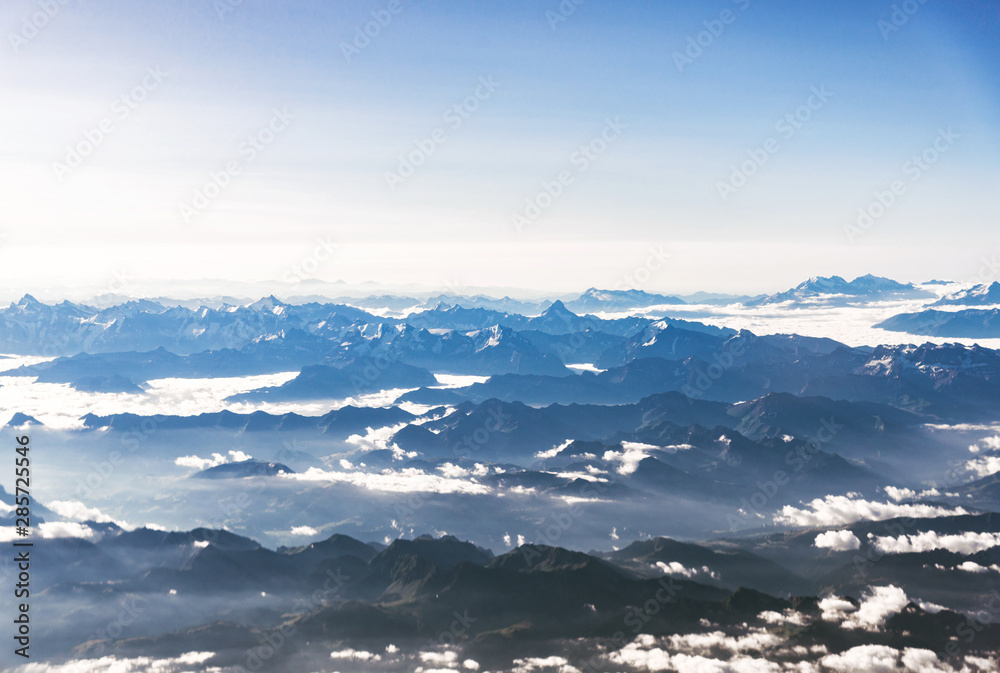 Landscape aerial view of colorful blue Alps mountains with clouds and fog above Switzerland