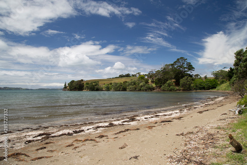 Algies Bay on Matakana coast near Snells Beach. Sunny day after a storm. Seaweed and debris washed up on shore. Clouds in sky, summers day. Nice small bay sheltered for swimming, boating and water fun