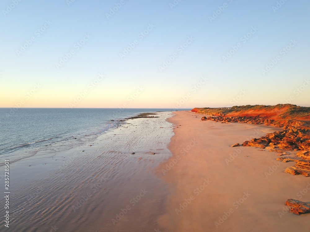 Scenic aerial panoramic view of remote coast near Broome, Western Australia, with ocean, beach, red cliffs, outback landscape and sunset blue sky as copy space.