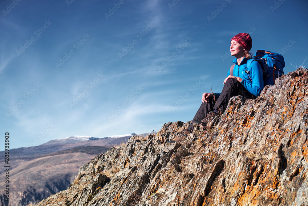 Hiker woman with backpack sitting on rock of a mountain and enjoying sunrise