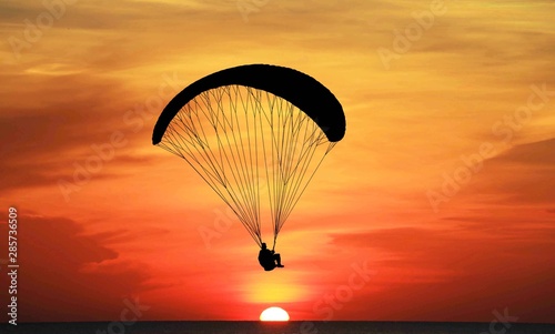 silhouette paraglider flying on sunrise