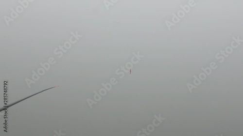 Fisherman on a lake early in a misty morning fishing and draws a crucian from the water