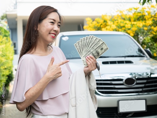 Asian woman holding money and car key against a car. insurance, loan and finance concept