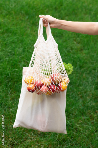 Female hand with cotton eco bag on green background. Zero waste concept