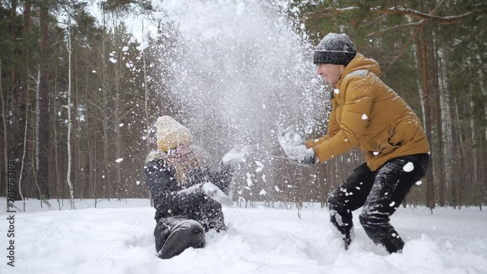 Young happy couple, man and woman, are having a fun time throwing a snow each other in winter forest in slow motion. Family weekend.