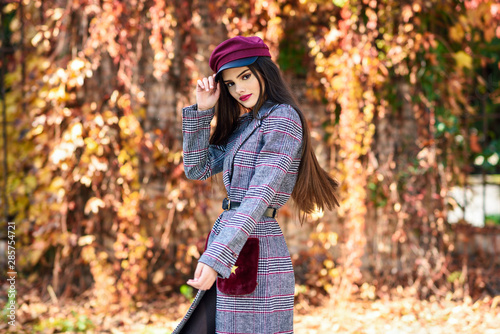 Young beautiful girl wearing winter coat and cap in autumn leaves background.