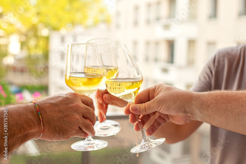 People hands cheering with white wine glases on the terrace. Summer aperitif with group of friends.
