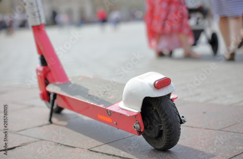 Electric scooter parked in city center, sunny summer day, behind people and buildings in soft focus