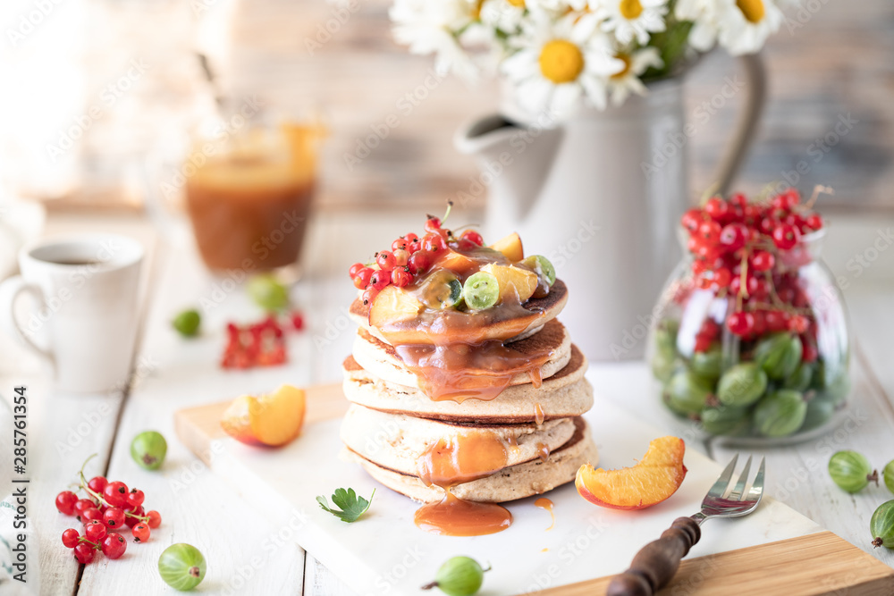Cornmeal pancakes with salted caramel served with berries and fruits on a white wooden background.