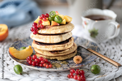 Cornmeal pancakes with honey, served with berries and fruits on a white wooden background.