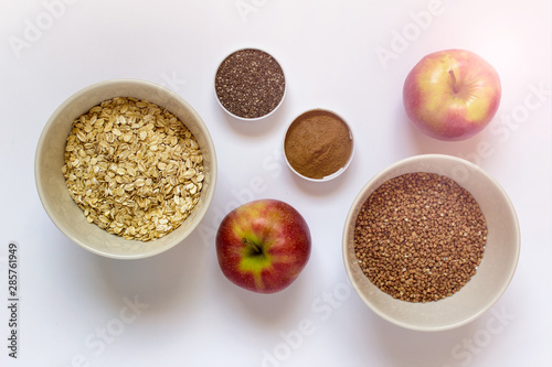 Healthy breakfast - apples, grains , oats, buckwheat, cinnamon, chia seeds on white background. © dariaren