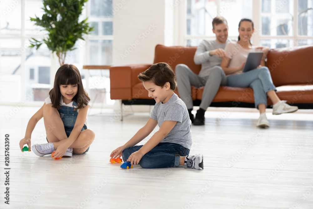 Obraz premium Parents relaxing using device on sofa, kids play on floor